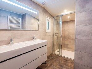 Ein modernes Badezimmer mit großem Spiegel, zwei Waschbecken, einer Duschkabine und Fliesenboden.
