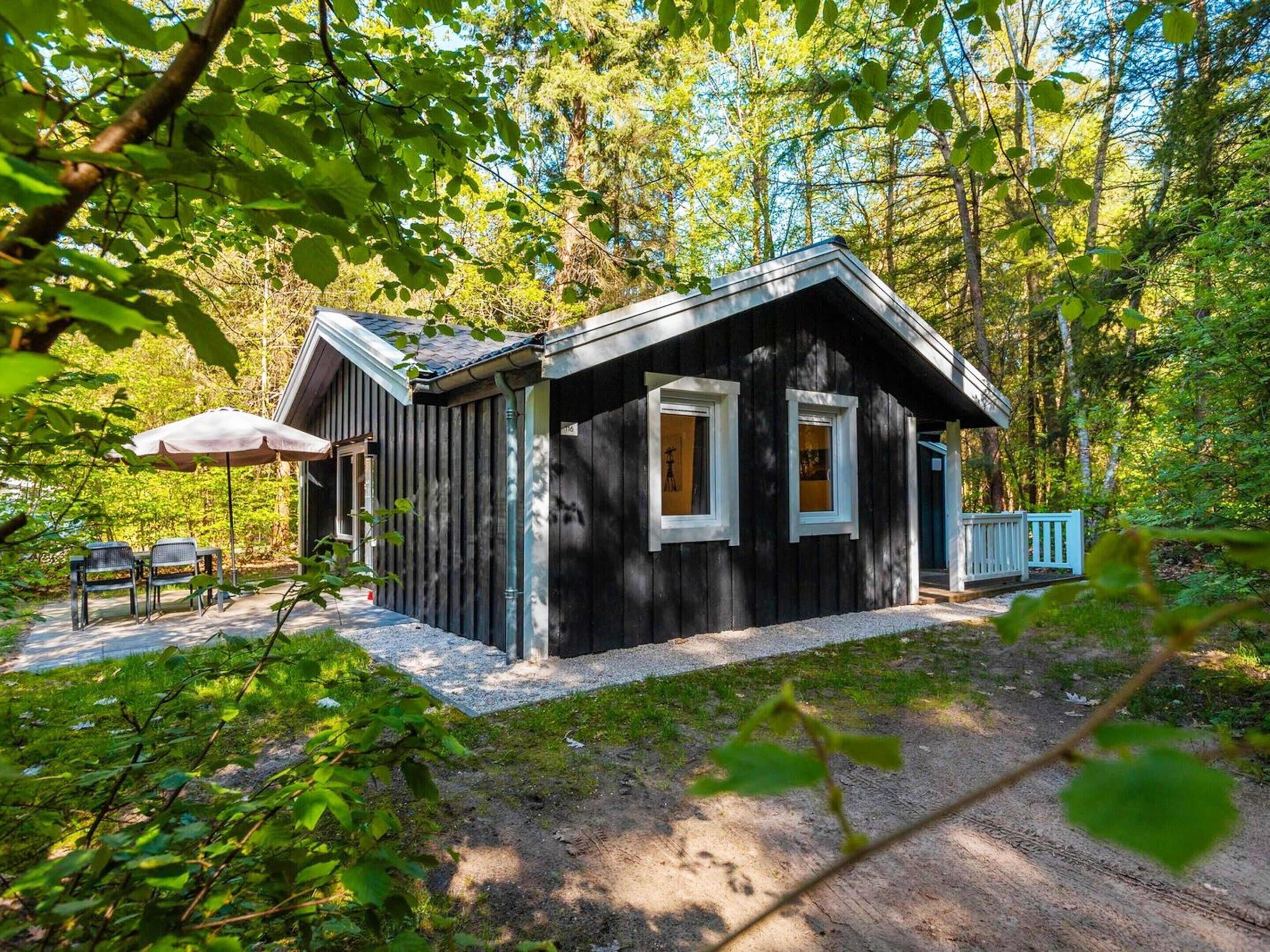 Eine Hütte mit Veranda, einem Tisch und Stühlen sowie einem weißen Zaun.