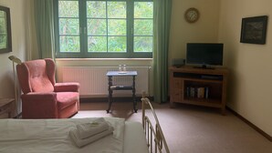 A hotel room with a bed, a chair, a table with a lamp, a television, and a window with curtains. - Apartment '6 Ground Floor' with Shared Garden (Südmüritz)