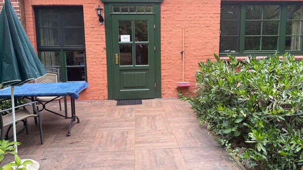 A brick building with a green door, a blue table, and a green umbrella. - Apartment '6 Ground Floor' with Shared Garden (Südmüritz)