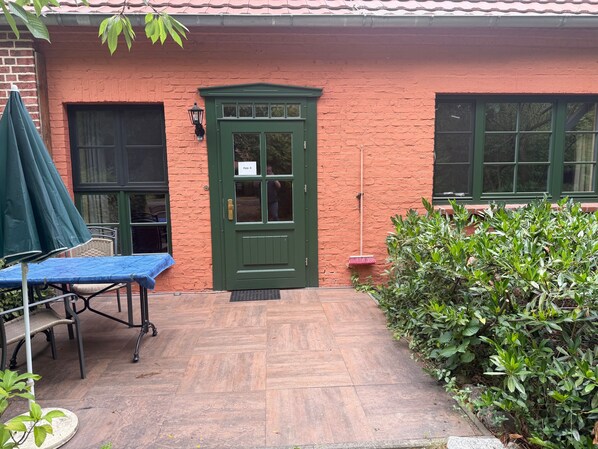 Un bâtiment en briques avec une porte verte, une table bleue et un parapluie vert.
