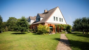 A two-story house with a sloped roof, a visible chimney, and a paved pathway leading to the entrance. - Apartment '6 Ground Floor' with Shared Garden (Südmüritz)