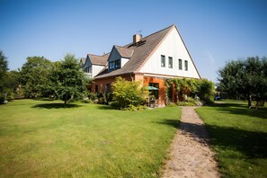 Une maison à deux étages, dotée d’un toit en pente, d’une cheminée bien visible et d’un chemin pavé menant à l’entrée.