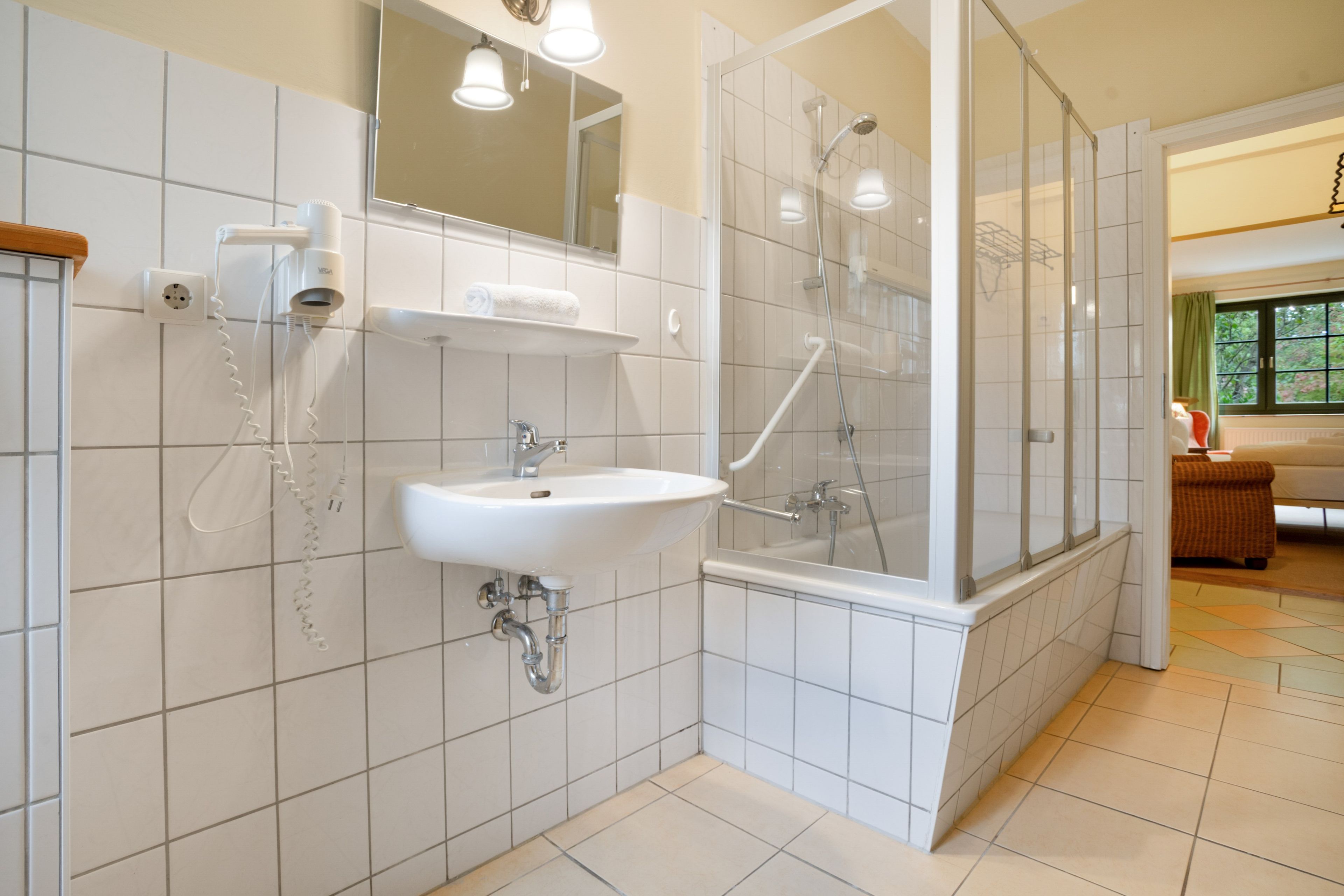 Ein Badezimmer mit weißem Waschbecken, Spiegel und Duschbereich.
