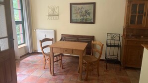 A room with a wooden table and chairs, a radiator, a window with curtains, a wall-mounted picture, and a wooden cabinet. - Apartment '6 Ground Floor' with Shared Garden (Südmüritz)