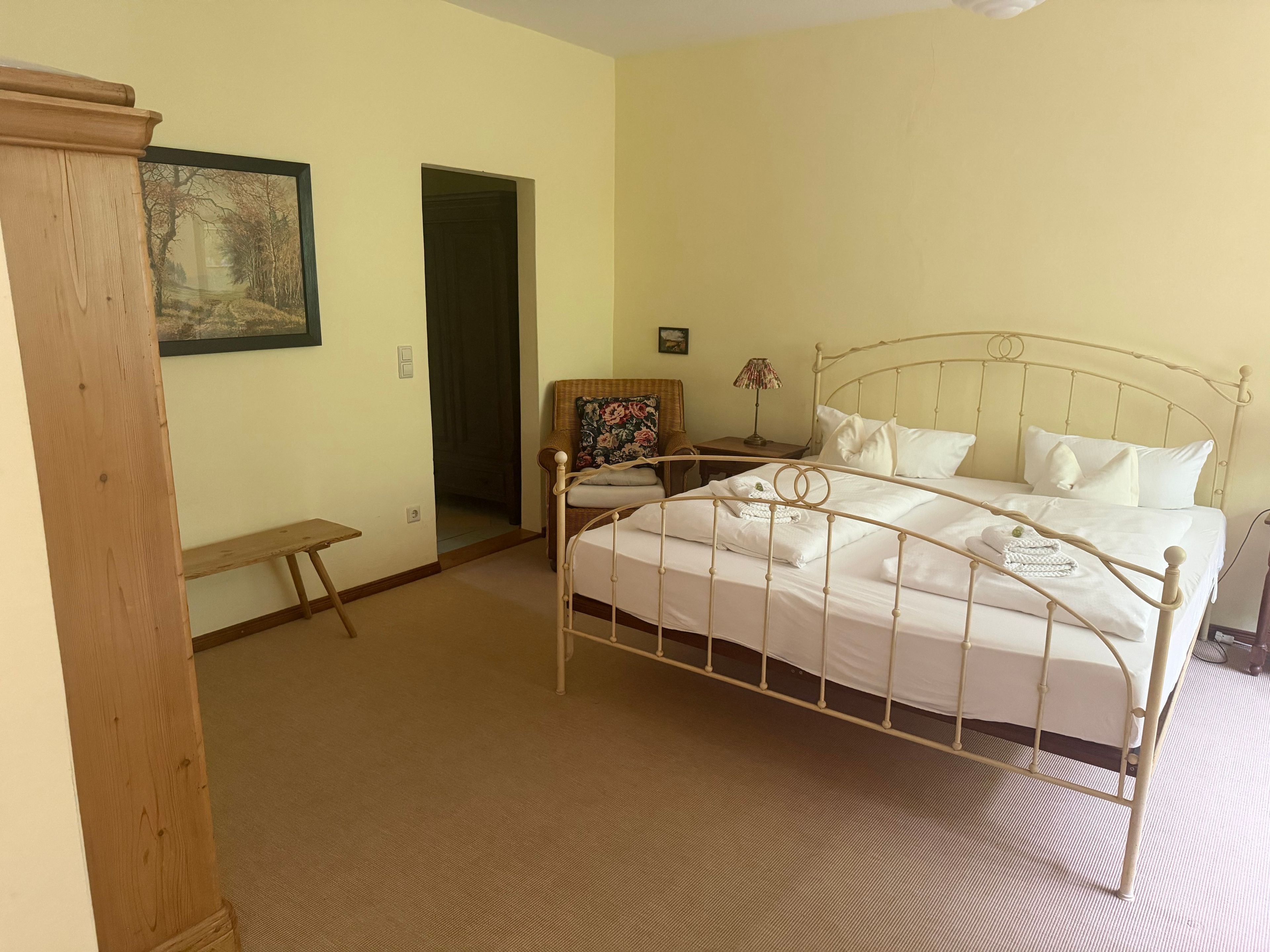 A bedroom with a single bed, a chair, a small table, and a door leading to another room.