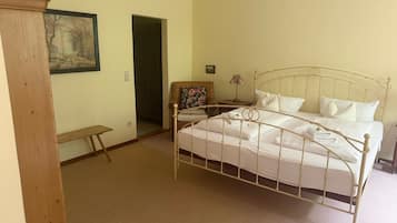 A bedroom with a single bed, a chair, a small table, and a door leading to another room.