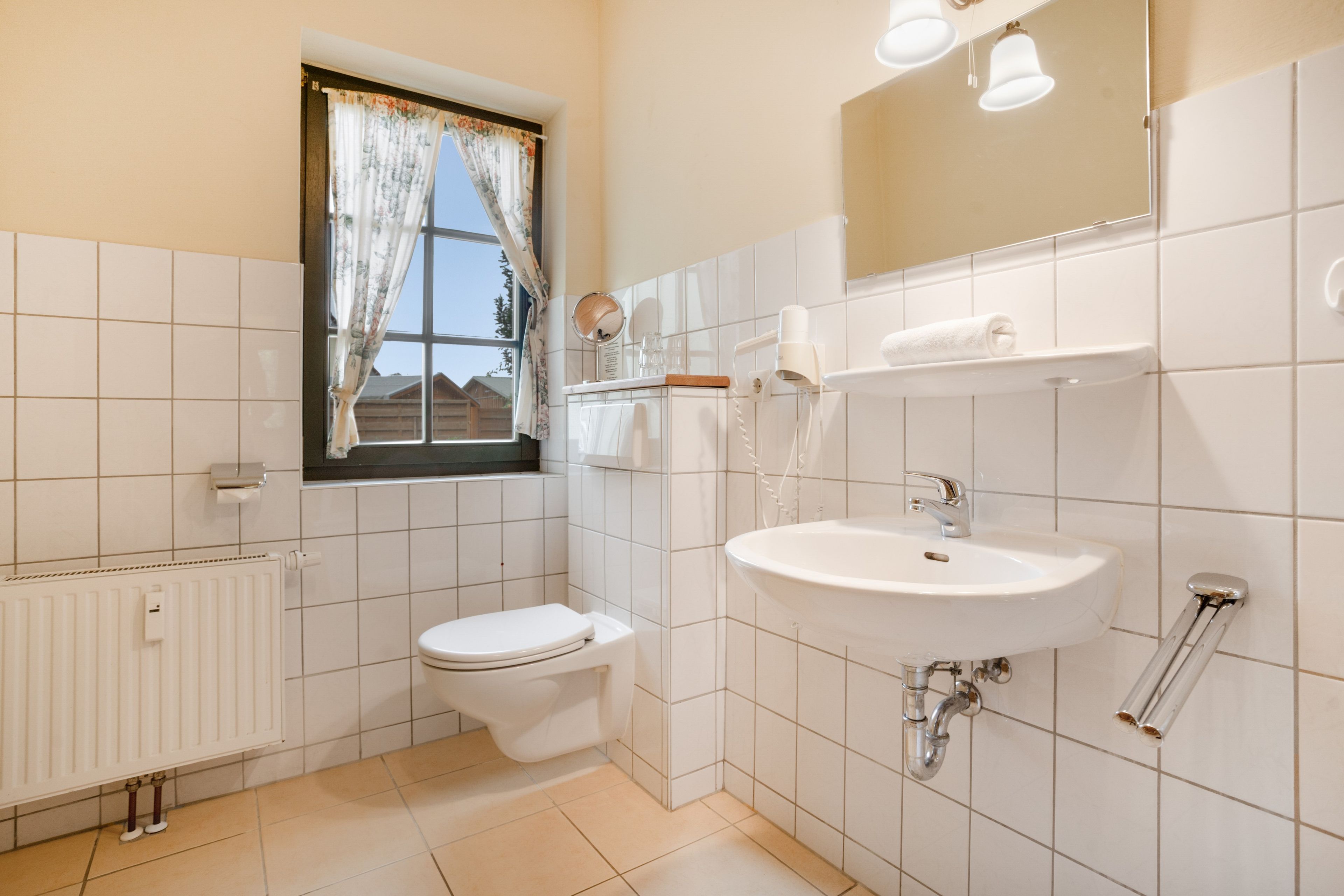 Ein Badezimmer mit Toilette, Waschbecken und einem fenster mit Vorhängen.
