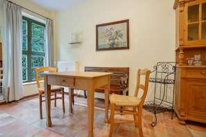 A dining area with a wooden table and chairs, a window with curtains, a radiator, a painting on the wall, and a wooden cabinet. - Apartment '6 Ground Floor' with Shared Garden (Südmüritz)