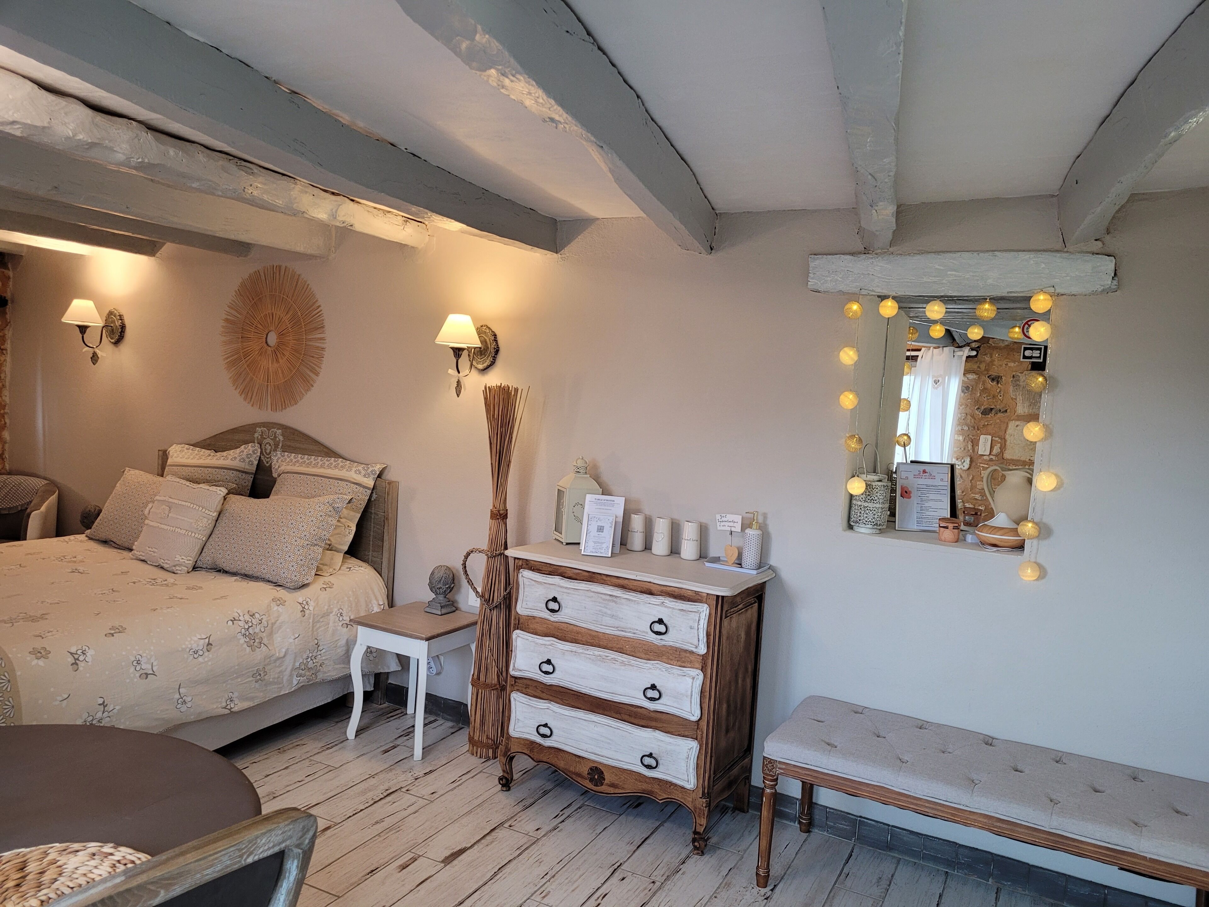A bedroom with a bed, bedside table, dresser, lamp, mirror, and wall sconces.