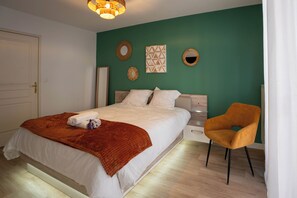 Un dormitorio con cama, una silla, mesita de noche y adornos en la pared.