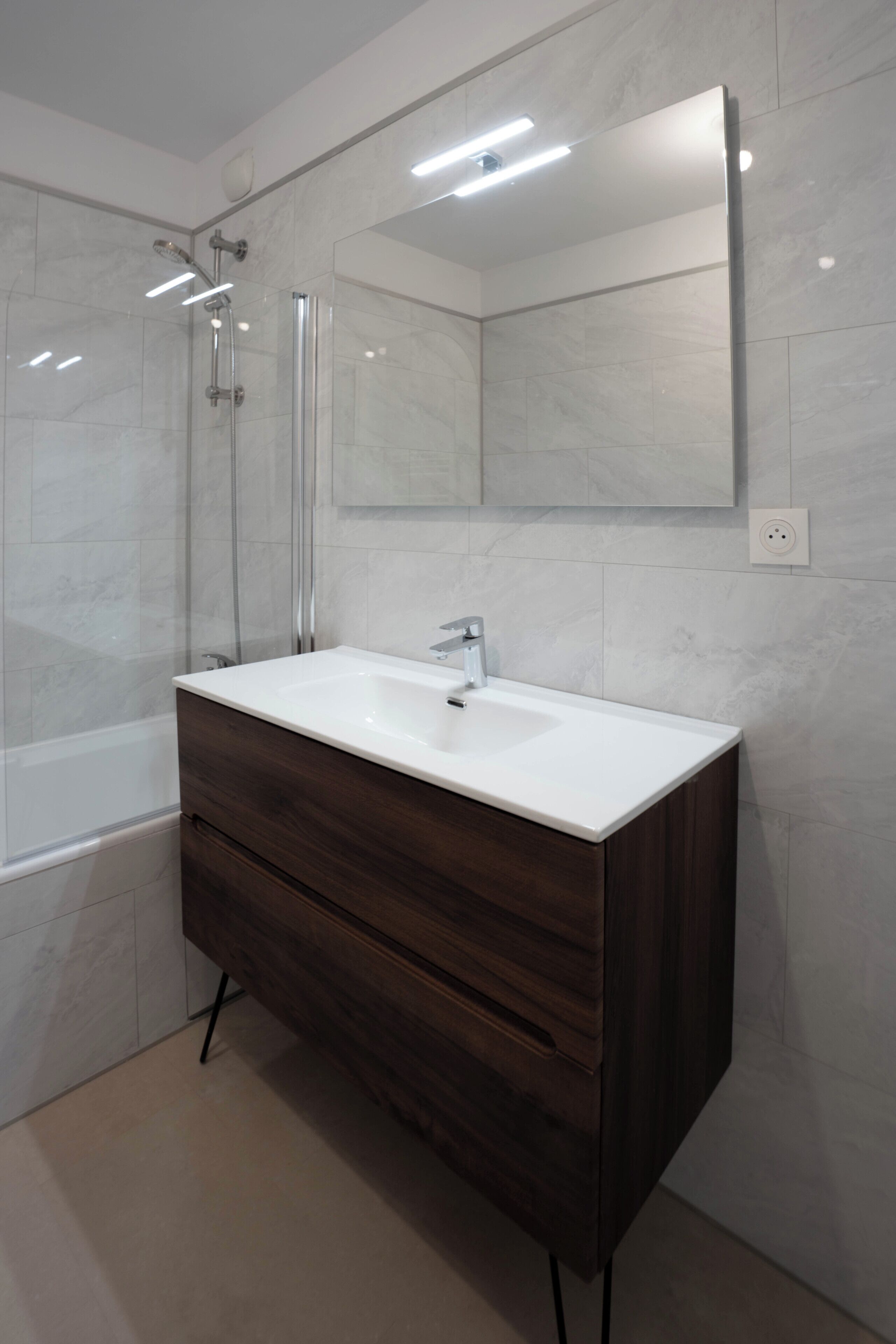 Une salle de bain moderne avec un meuble-lavabo blanc, une cabine de douche en verre et un grand miroir.