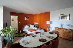 A modern hotel room with a bed, a dining table set for two, and a small desk with a lamp. - 2-bedroom apartment - sleeps 7 with balcony / 15 min from Lyon / 5 min from Doua (Villeurbanne)