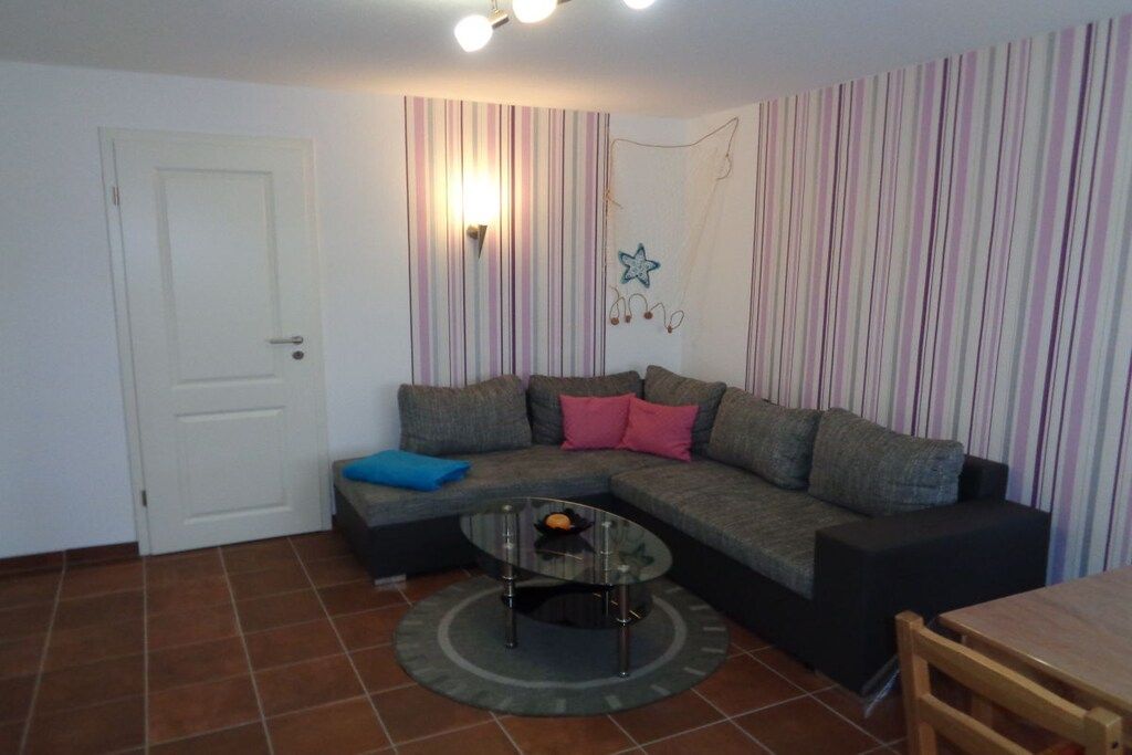 Een woonkamer met een hoekbank, een glazen salontafel, een deur en een gestreepte wand.