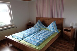 Ein Einzelbett mit Holzrahmen, ein Nachttisch, eine Lampe und ein Fenster mit Jalousien.