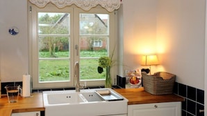 A kitchen with a double sink, a lace window valance, a vase with flowers, a candle, and a basket on the counter. - on the hereditary village headman's farm (Buchholz)