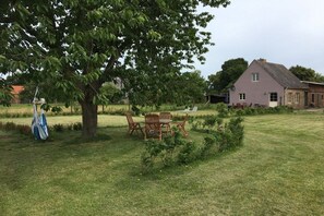 Eine grüne Außenanlage mit Picknicktisch und Stühlen, einem großen Baum und einem Haus im Hintergrund.