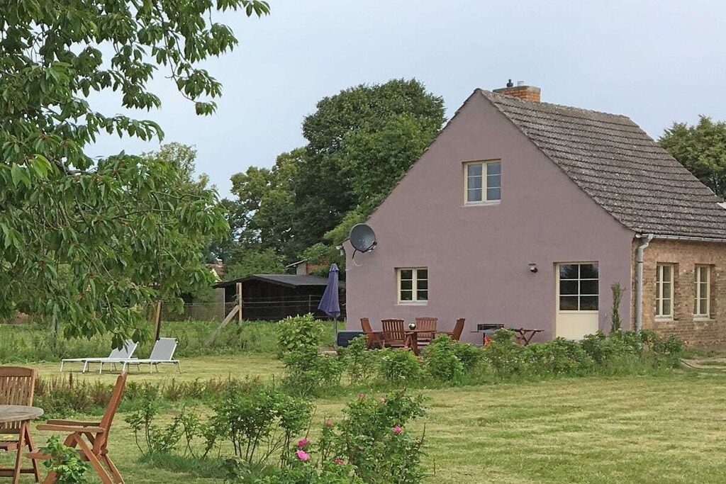 Una casa con antena parabólica, un espacio exterior techado y un césped con sillas.