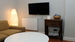 A living room with a sofa, a white coffee table, a television mounted on the wall, a radiator, and a wooden side table with a bowl. - on the hereditary village headman's farm (Buchholz)