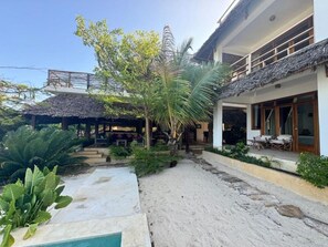 A resort with a pool, outdoor seating, and a covered area with a thatched roof. - Palafitta Zanzibar (Pingwe)