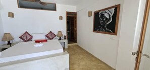 Een hotelkamer met een bed, een schilderij aan de muur en een deur naar een andere kamer.