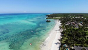 A coastal area with a beach, clear waters, and a dense cluster of buildings. - Palafitta Zanzibar (Pingwe)