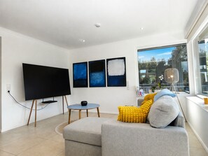 A modern living room with a flat-screen TV, a sofa with cushions, a small round table, and abstract wall art. - fewo1846 - Berglyk 1 - Beach House with a Rooftop Terrace, Garden, and 2 Bedrooms (Glücksburg)