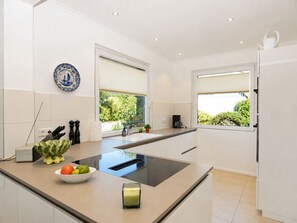 A modern kitchen with a central island, a built-in stove, and a window with a view of greenery. - fewo1846 - Berglyk 1 - Beach house with a rooftop terrace, garden, and 2 bedrooms (Glücksburg)