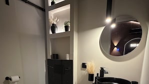 Ein modernes Badezimmer mit einem schwarzen Waschtisch, einem runden Spiegel und einer Toilette.