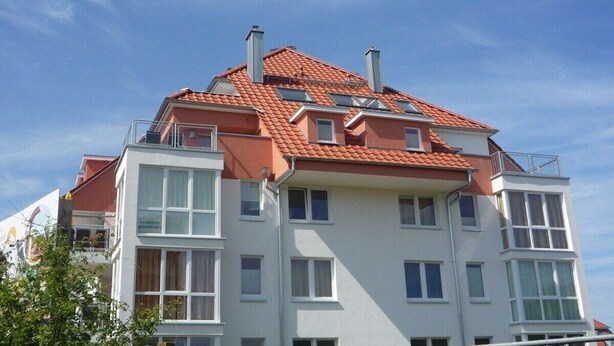 Ein mehrstöckiges Wohngebäude mit rotem Ziegeldach, weißen Wänden und zahlreichen Fenstern.