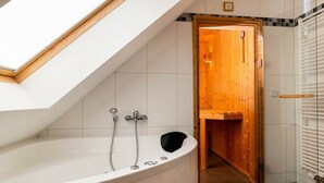 Ein modernes Badezimmer mit Oberlicht, einer freistehenden Badewanne und einer Holztür zum Duschbereich.