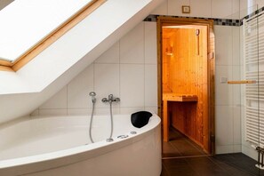 A modern bathroom with a skylight, a freestanding bathtub, and a wooden door leading to a shower area. - Holiday apartment with 3 bedrooms (Großenbrode)