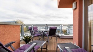 Ein Balkon mit Liegestühlen und einem Tisch mit Blick auf eine Stadtlandschaft.