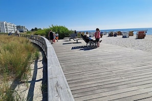 A wooden boardwalk leading to a beach with people walking, a wheelchair, and beach huts. - Holiday apartment with 3 bedrooms (Großenbrode)