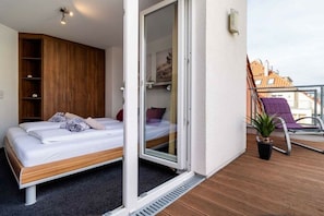 A bedroom with a bed, a wardrobe, and a sliding glass door leading to a balcony with a chair and a plant. - Holiday apartment with 3 bedrooms (Großenbrode)