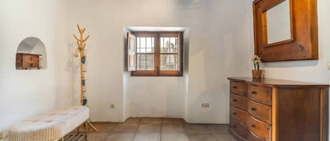 A room with a wooden dresser, a bench, a coat rack, a window, and a mirror on the wall.