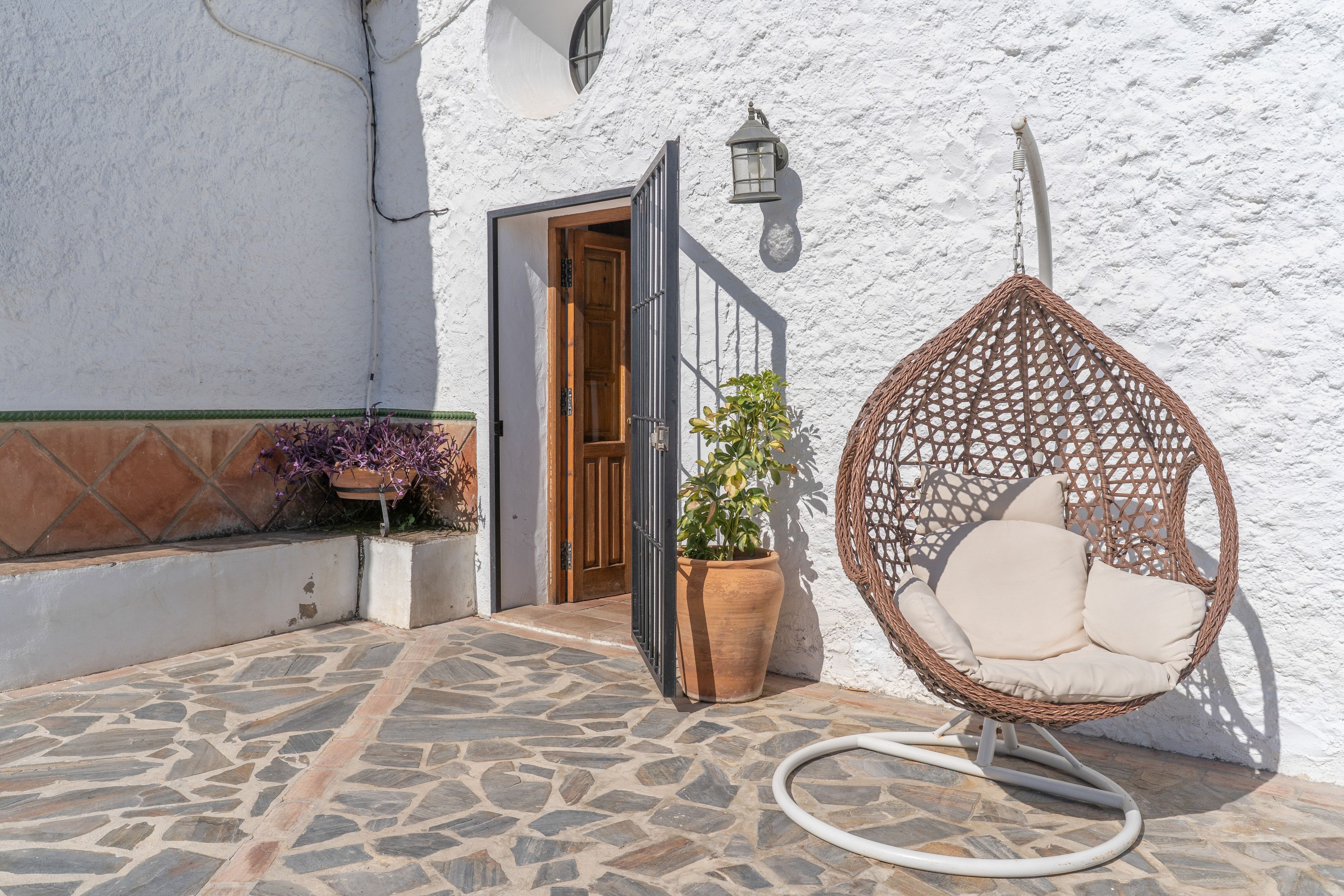 Un patio con baldosas de piedra, una mecedora de mimbre y una planta en maceta.