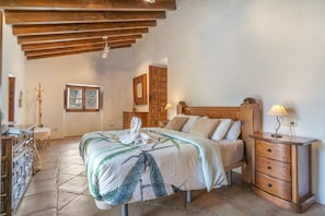 A bedroom with a wooden bed, bedside tables, a dresser, a window, and a wooden ceiling.