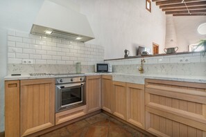 Une cuisine avec des carreaux de céramique blancs disposés en motif métro, un four encastré, des armoires en bois et une petite fenêtre.