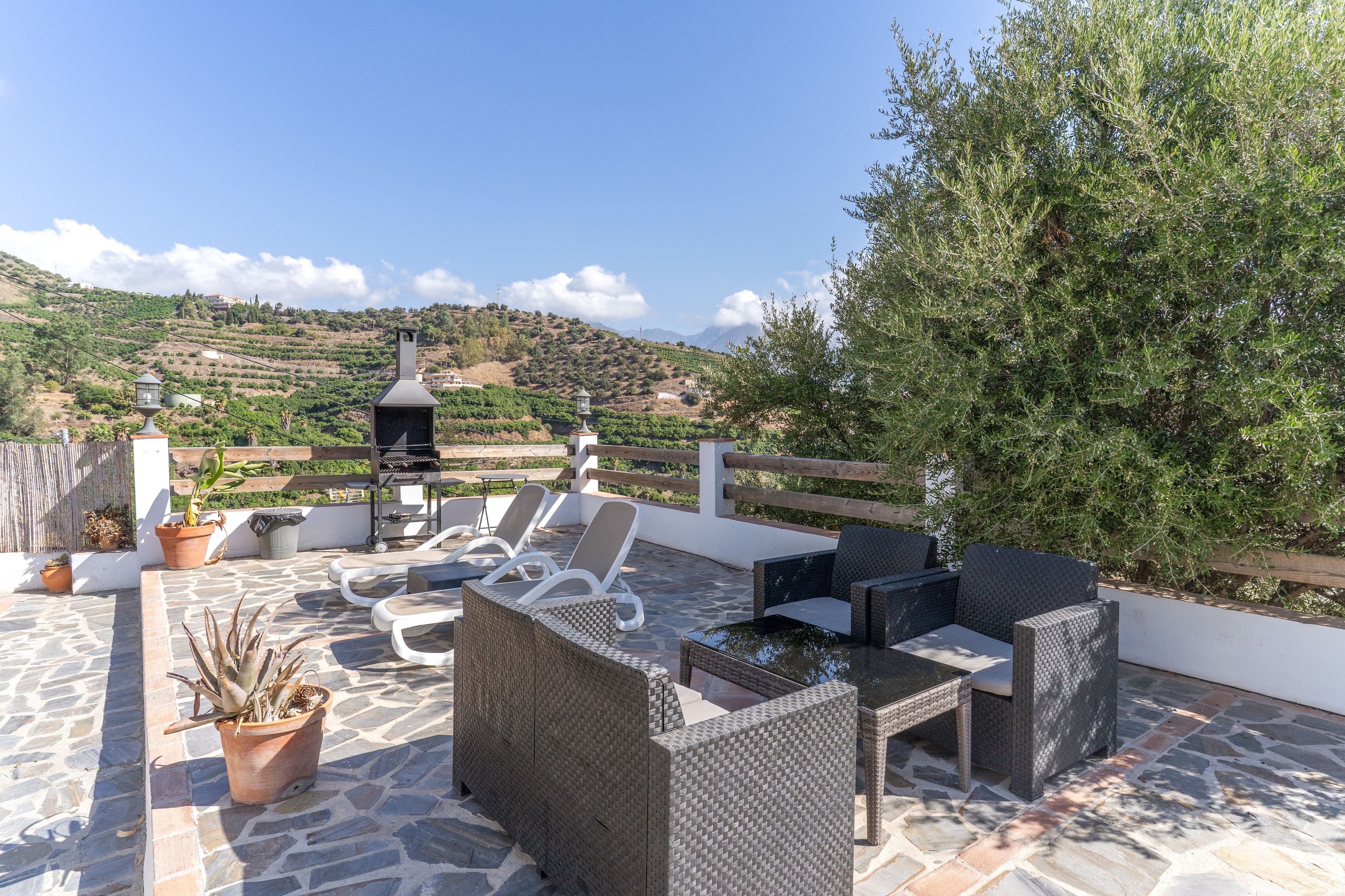 Un patio al aire libre con mobiliario de mimbre, una parrilla y plantas en macetas.