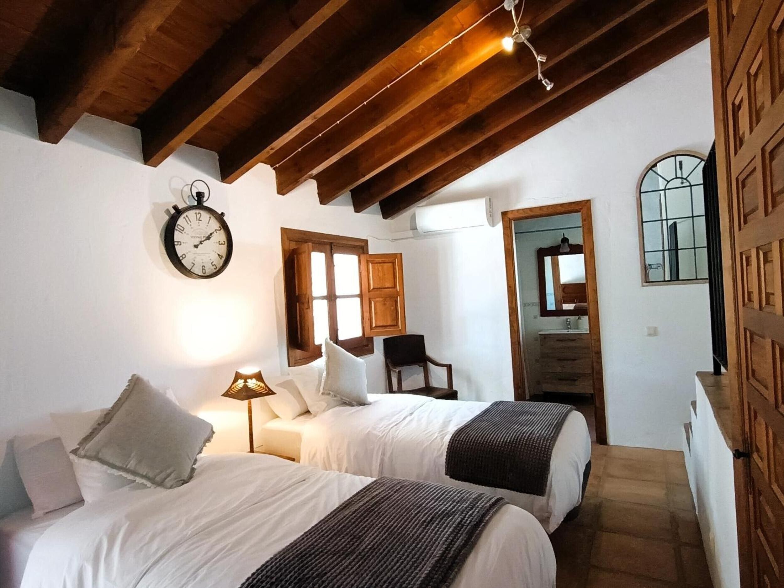 Un dormitorio con dos camas, techo de madera, un reloj y una ventana con vistas.