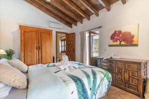 Een slaapkamer met een bed, een houten garderobe, een schilderij en een zichtbare badkamer door een geopende deur.
