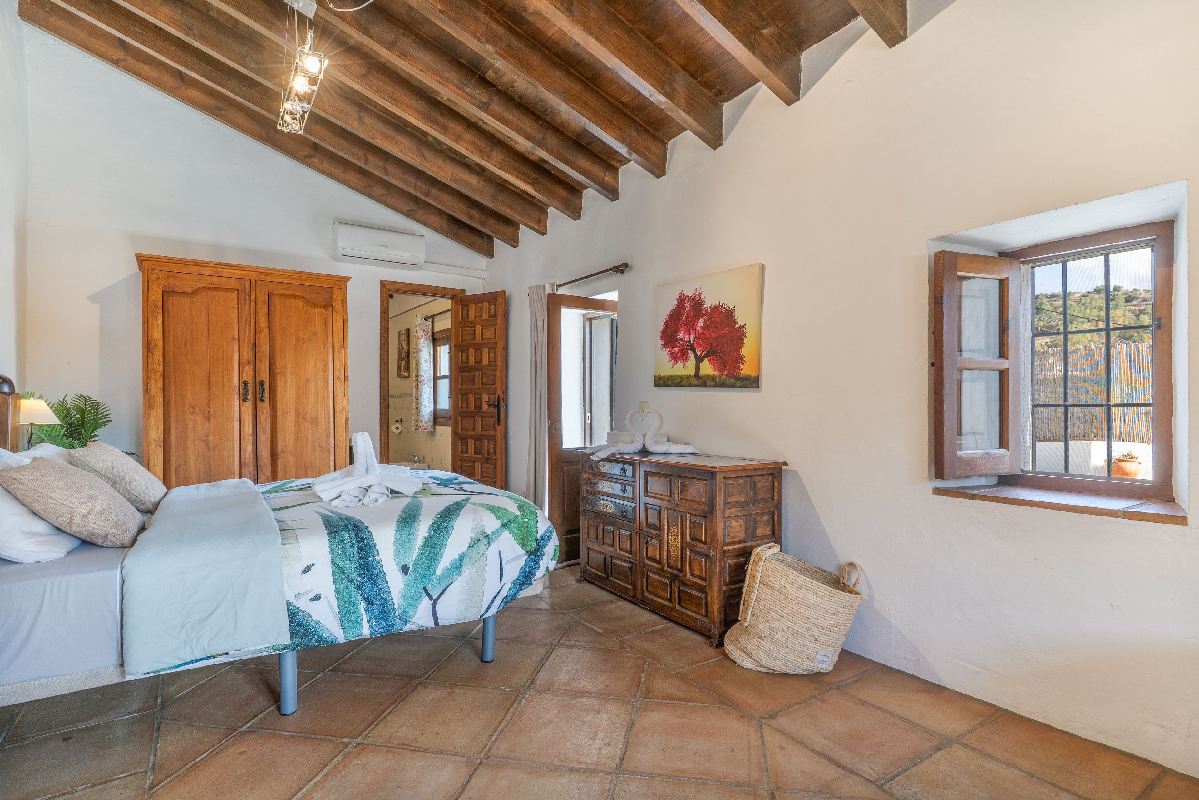 Un dormitorio con una cama, armario de madera, un cuadro, una ventana y una cesta de mimbre.
