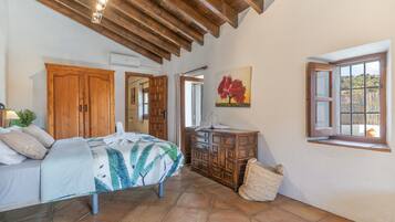 Un dormitorio con una cama, armario de madera, un cuadro, una ventana y una cesta de mimbre.