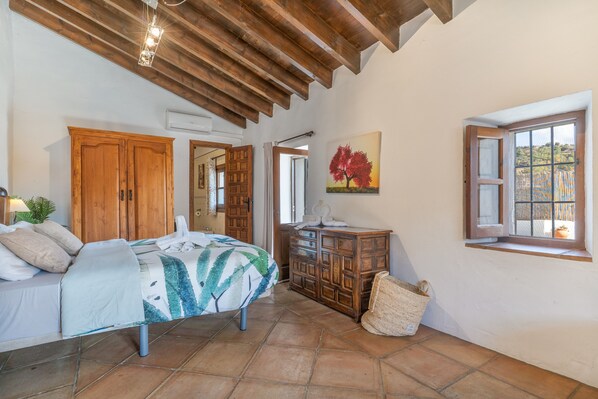 A bedroom with a bed, wooden wardrobe, a painting, a window, and a woven basket.