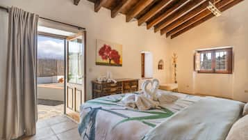 A bedroom with a large bed, a painting, a wooden dresser, and a view of the outdoors.