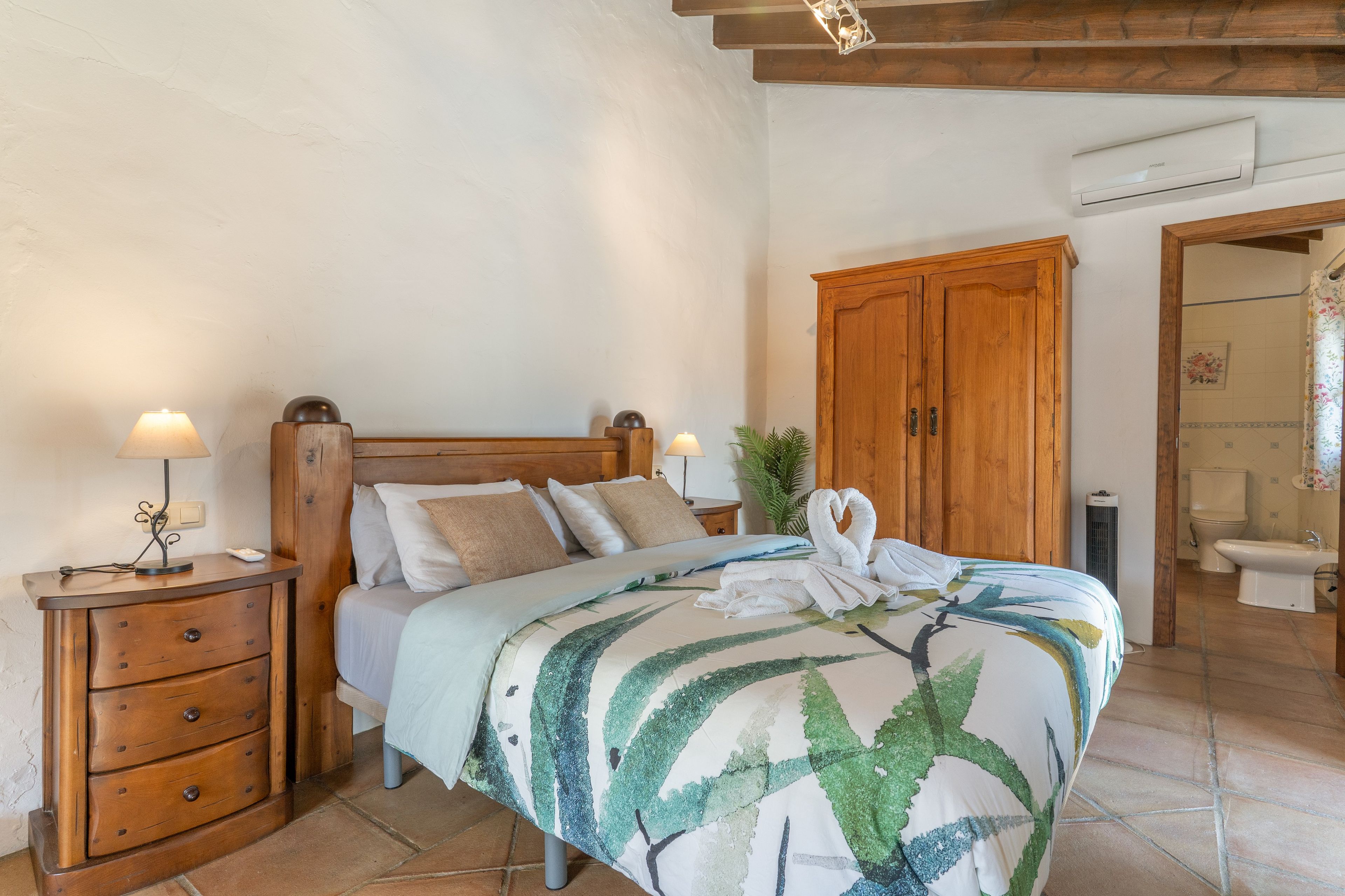 A bedroom with a wooden bed, bedside tables, a wardrobe, and a bathroom visible through an open door.