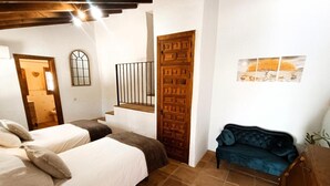 Une chambre avec deux lits, une porte en bois, un escalier et un canapé bleu.