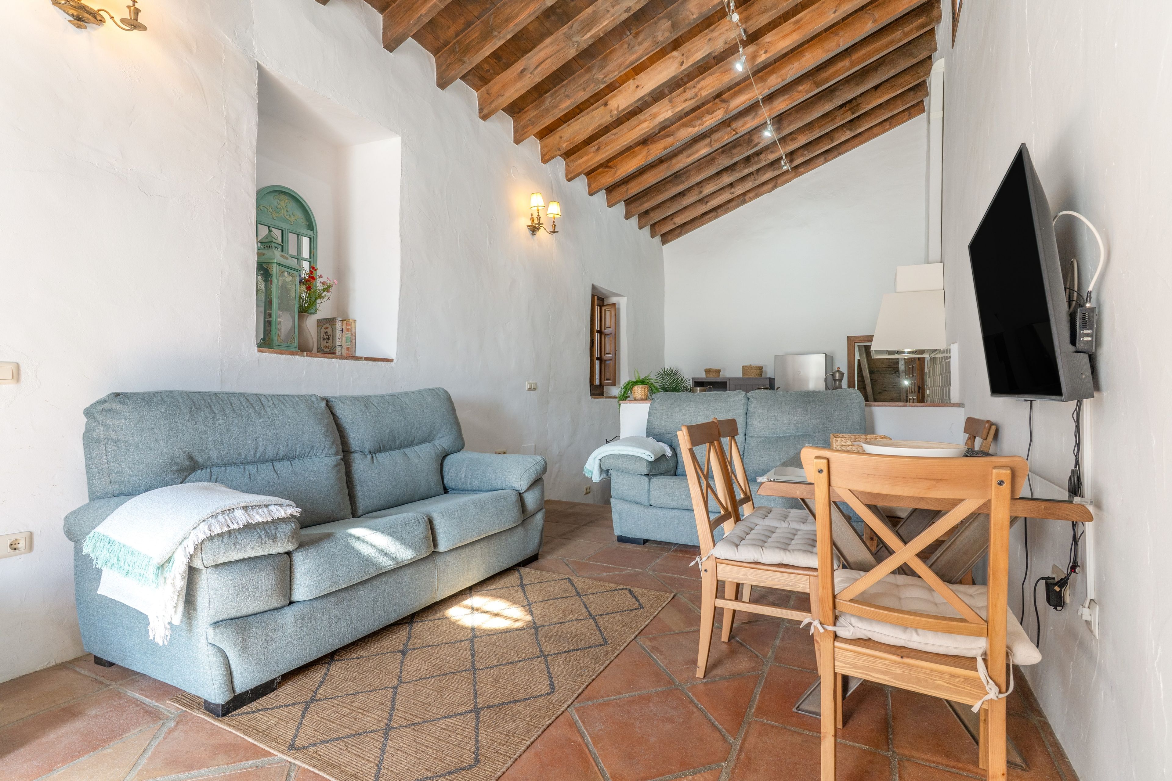 Un espacio de sala acogedor con un sofá, una mesa de comedor y un televisor montado en la pared.