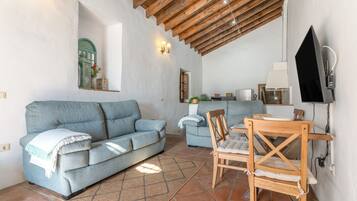 Un espacio de sala acogedor con un sofá, una mesa de comedor y un televisor montado en la pared.